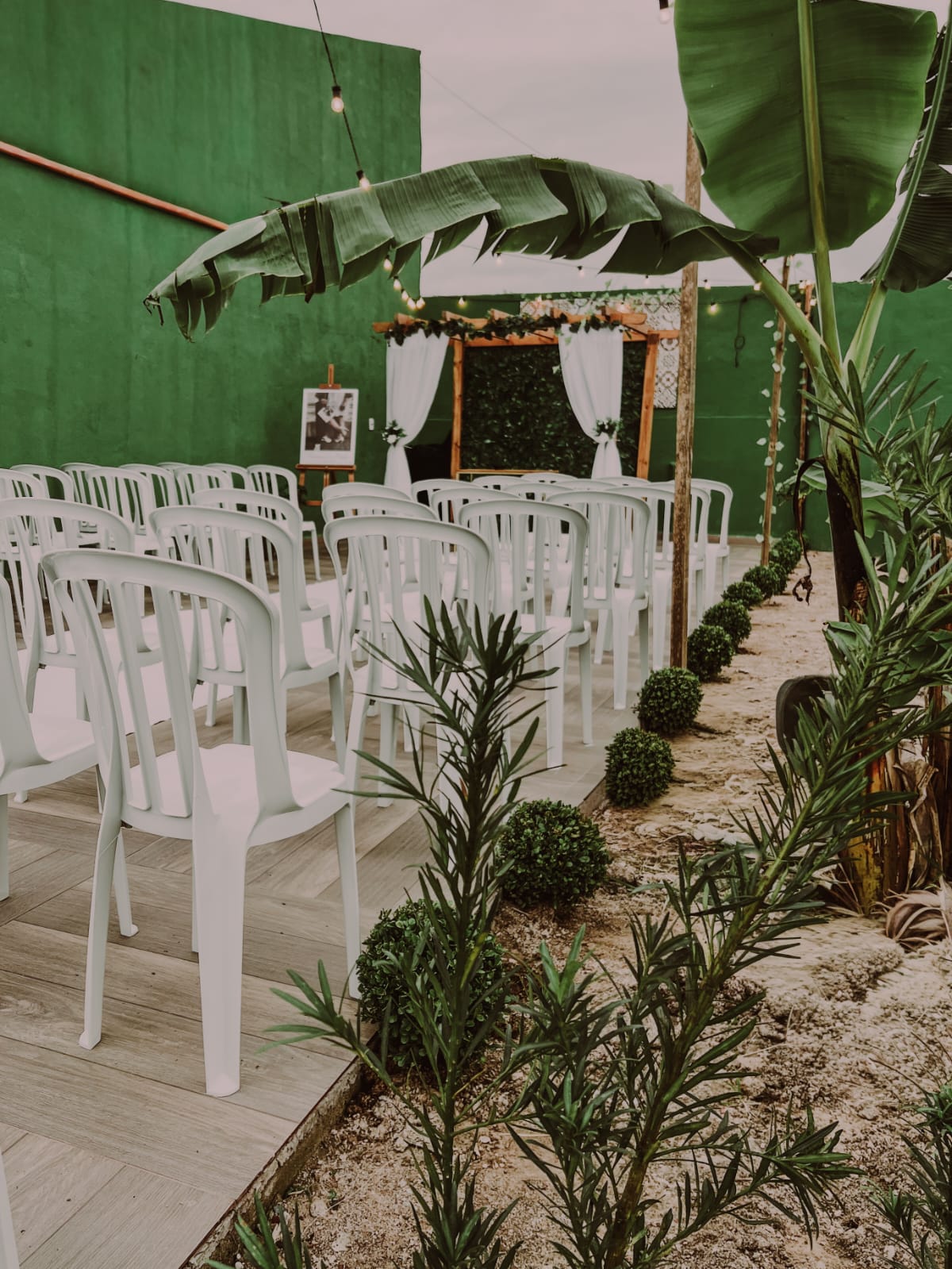 Espaço de cerimônia ao ar livre com cadeiras brancas e jardim
